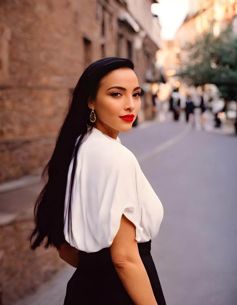 Dark-haired woman in red lipstick and white blouse on city street