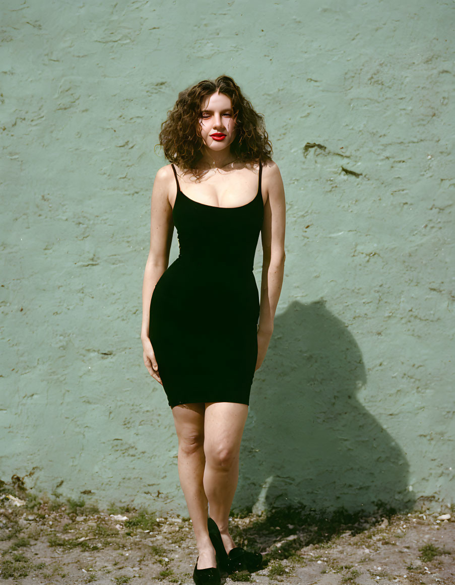 Woman in black dress against light green wall with shadow cast by sunlight