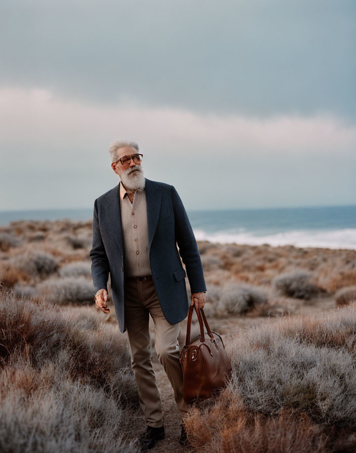 Elderly man with beard and glasses in blue blazer walking in coastal landscape