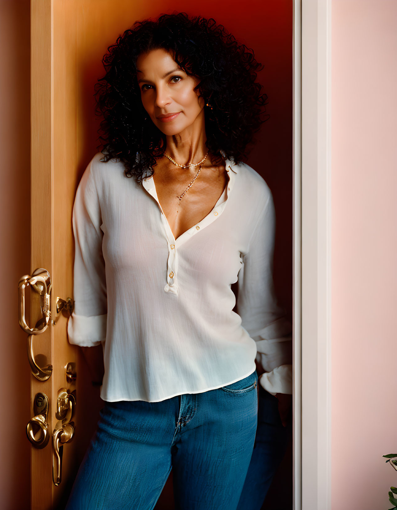 Curly-Haired Woman in White Blouse and Jeans by Open Door with Golden Light