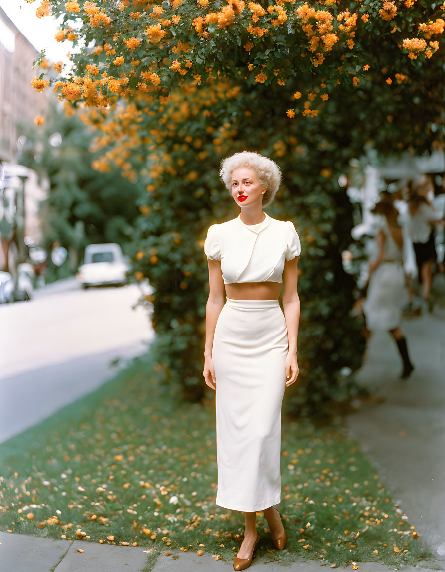 Blonde woman in white outfit on sidewalk with flowers