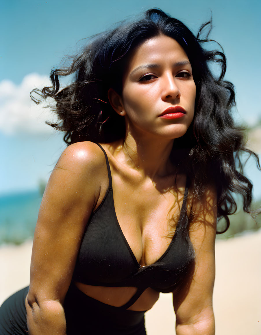 Woman with Long Dark Hair and Red Lipstick in Black Top on Beach Background