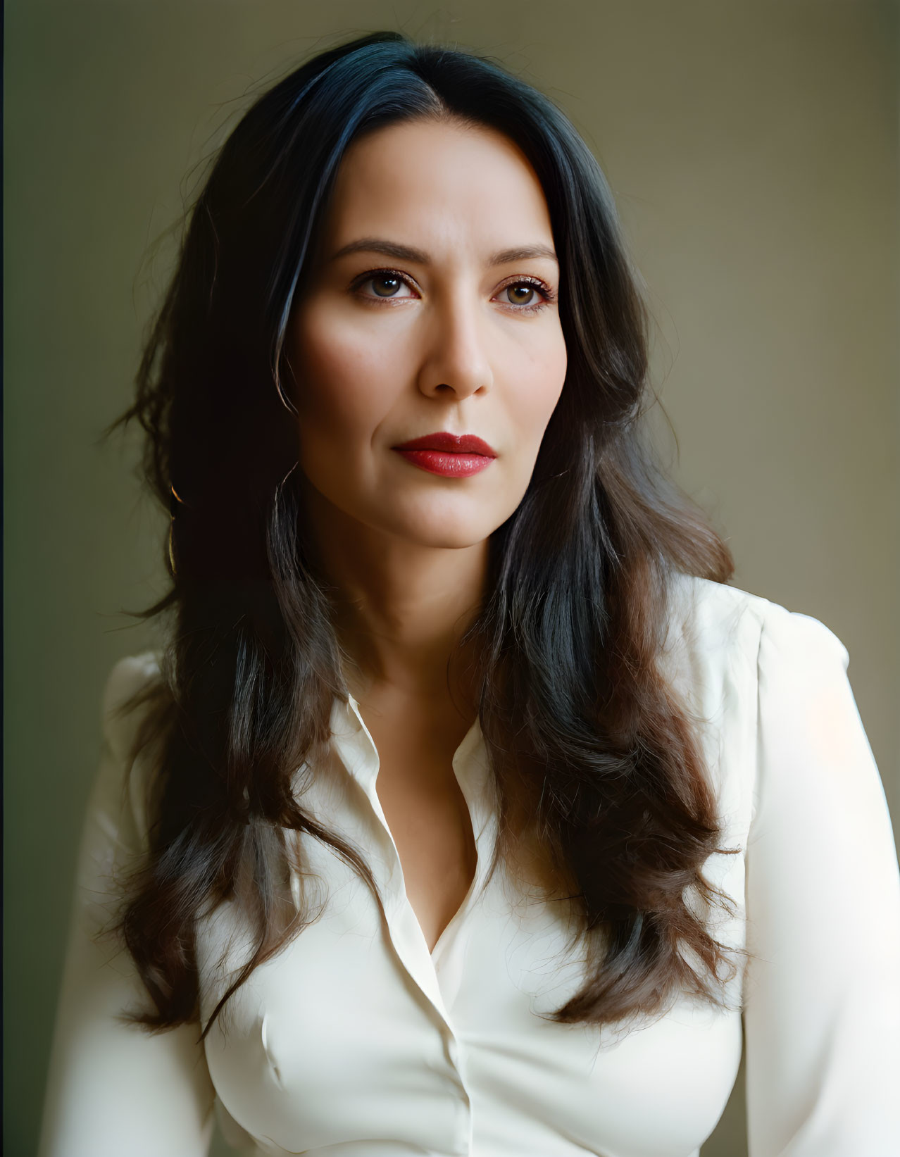 Portrait of woman with long dark hair in white blouse, gazing thoughtfully.