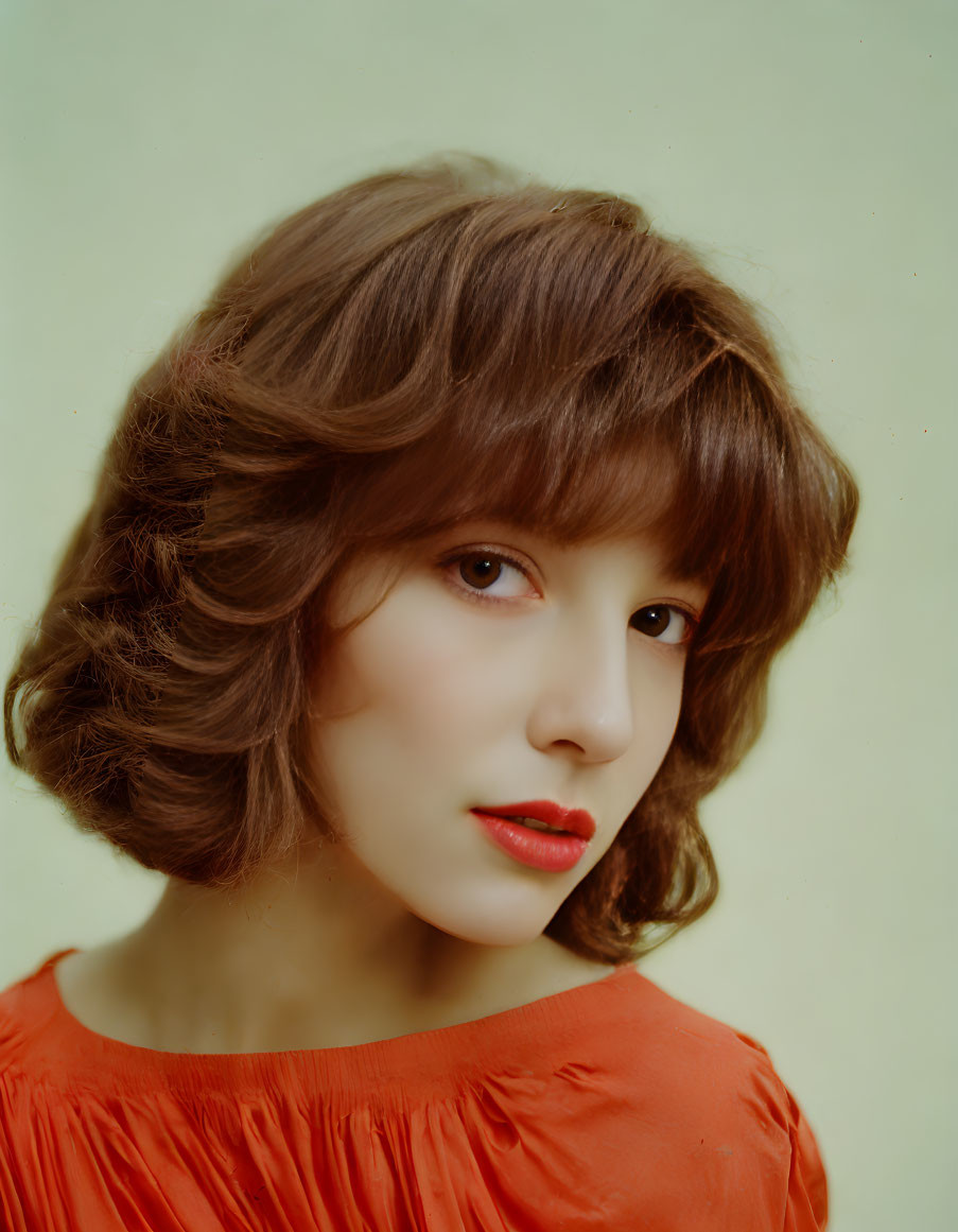 Woman with Chestnut Hair and Red Lipstick in Orange Blouse on Pale Green Background