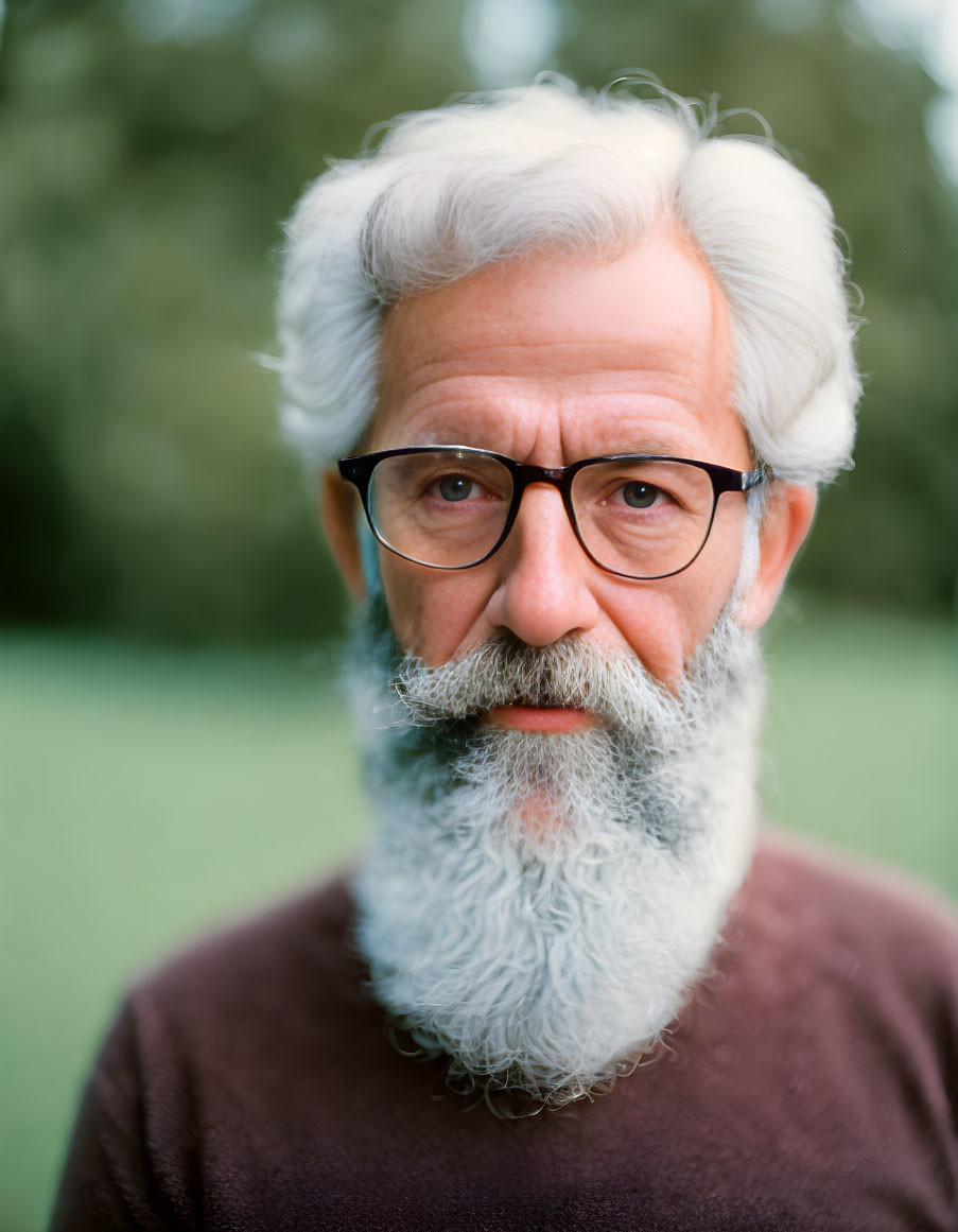 Elderly man with white beard and glasses in brown shirt on green background