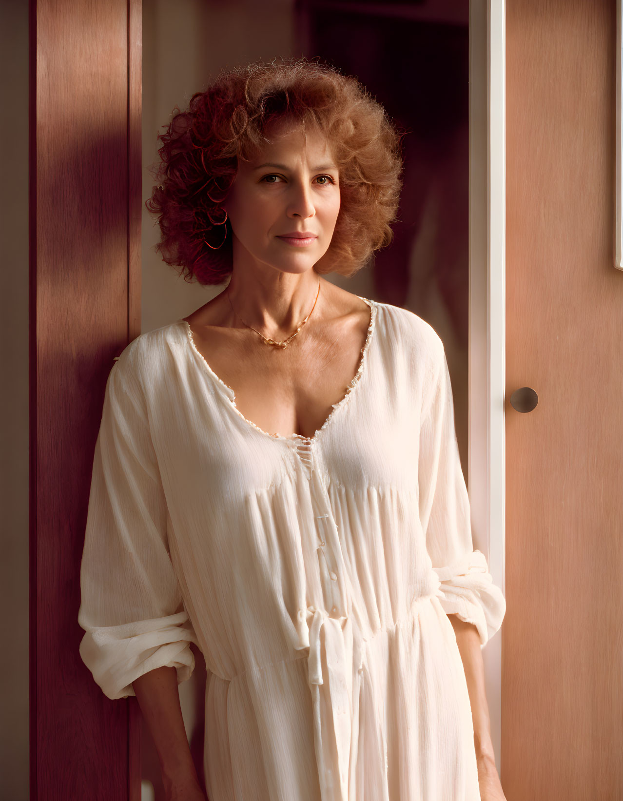 Curly-haired woman in white dress by door with soft lighting