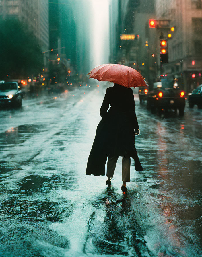 Person with red umbrella in rain-soaked street with city traffic.