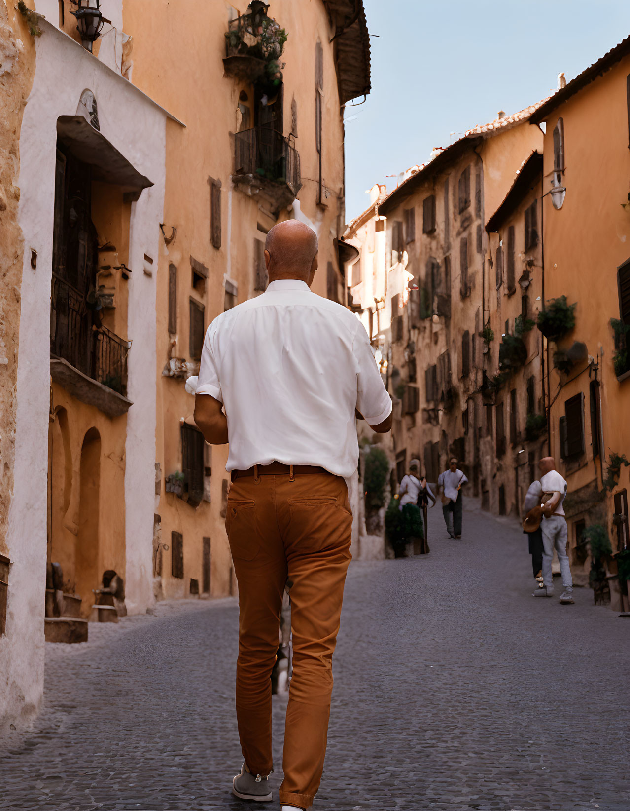 Bald man in white shirt walks down cobblestone street