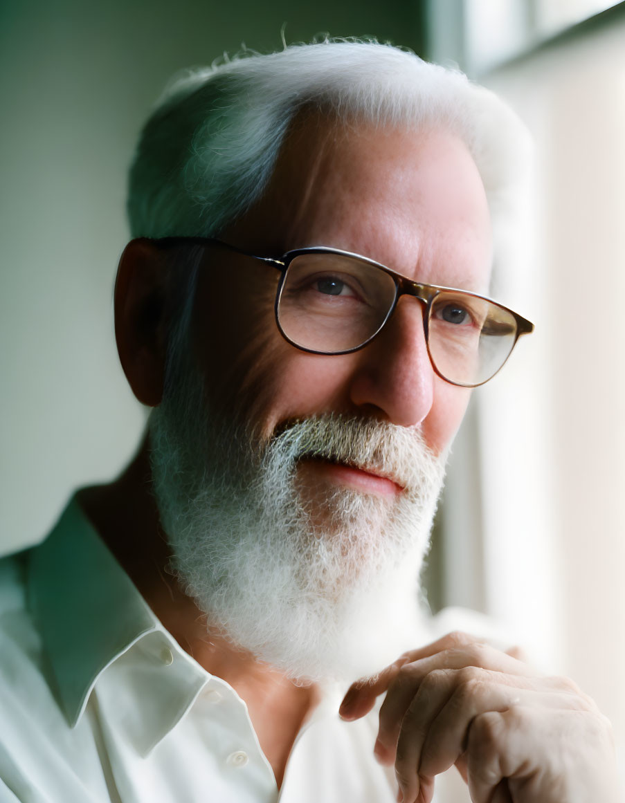 Elderly man with white beard and glasses smiling gently in softly lit setting