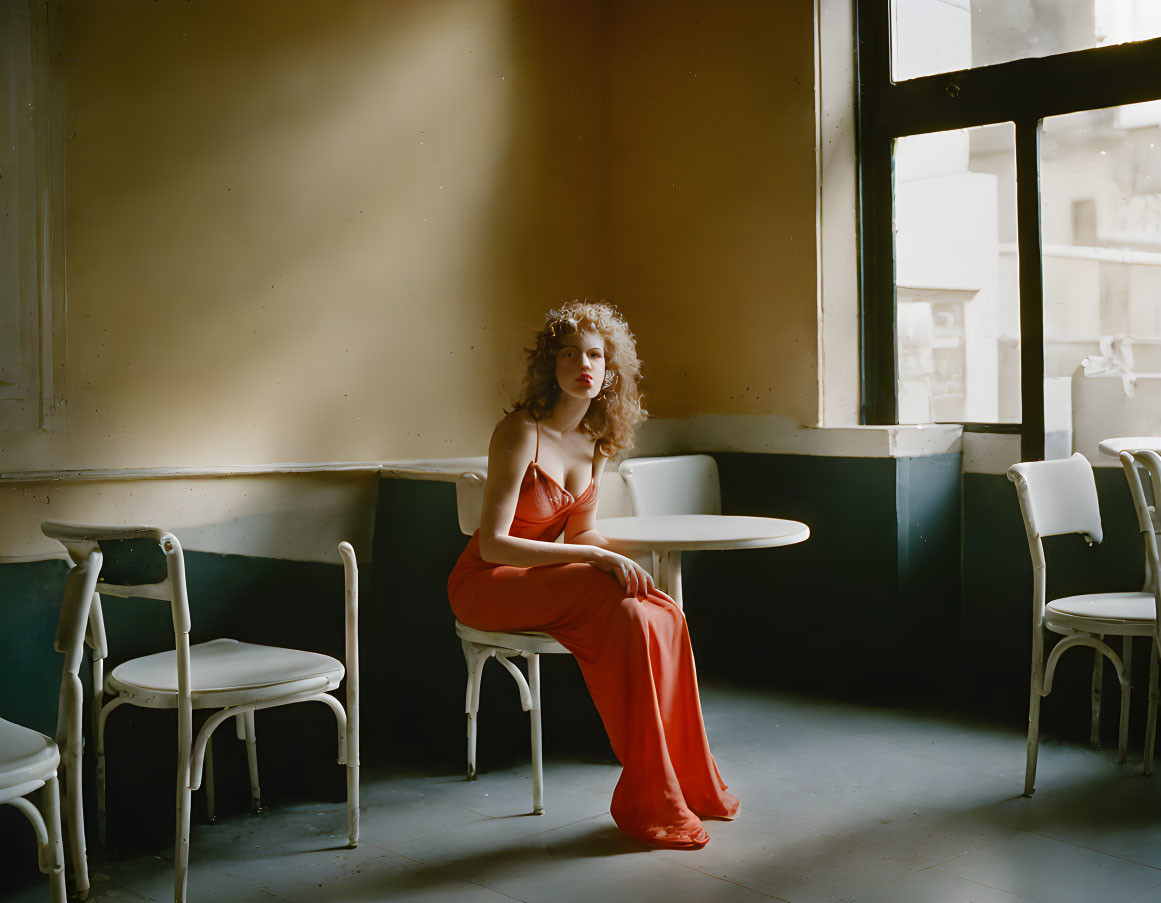 Woman in Red Dress Sitting at Table in Sunlit Room with White Chairs