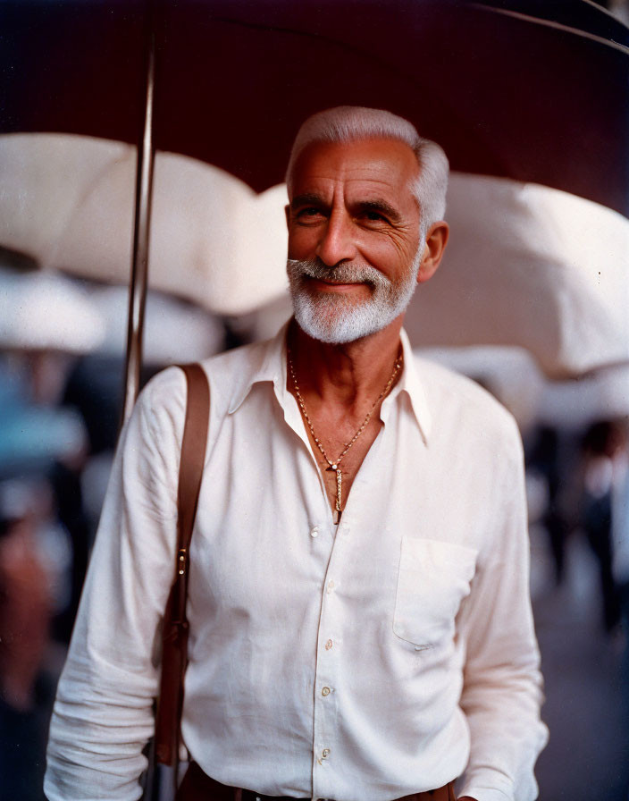 Elderly man with white beard and shirt smiling under umbrellas on busy street