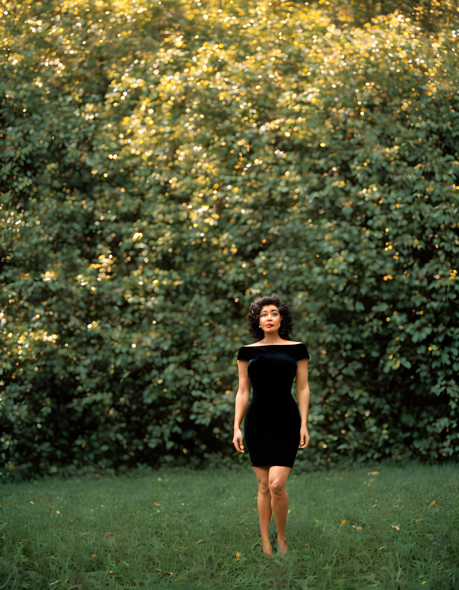 Person in Black Dress Standing in Front of Lush Green Backdrop with Yellow Flowers