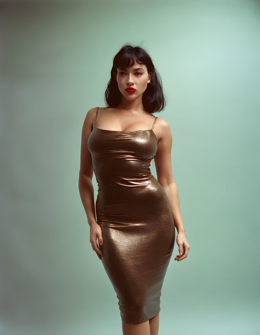 Dark-haired woman in red lipstick wearing metallic gold dress on soft green backdrop