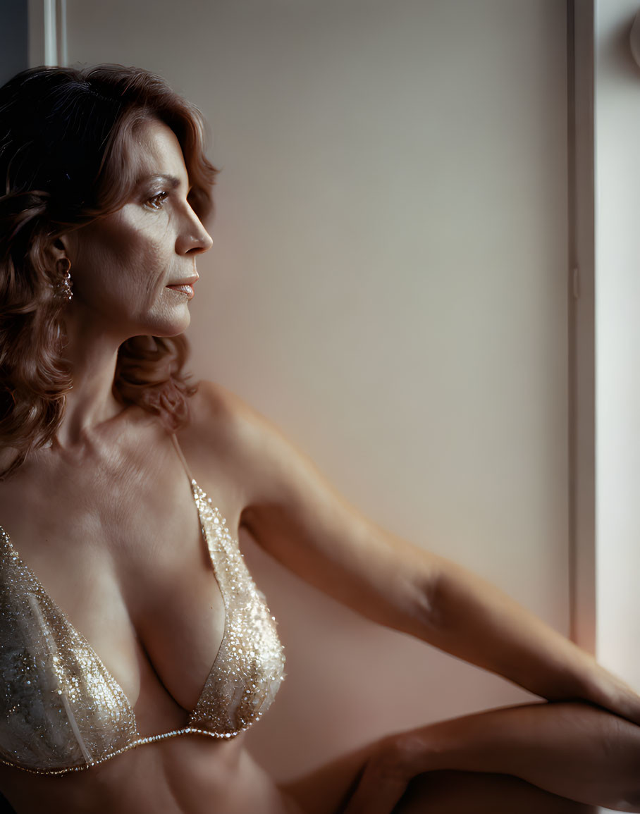 Contemplative woman in beaded top near window with soft light