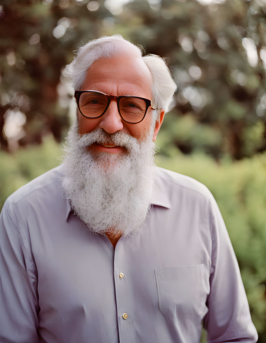 Elderly man with white beard and glasses smiling in light blue shirt