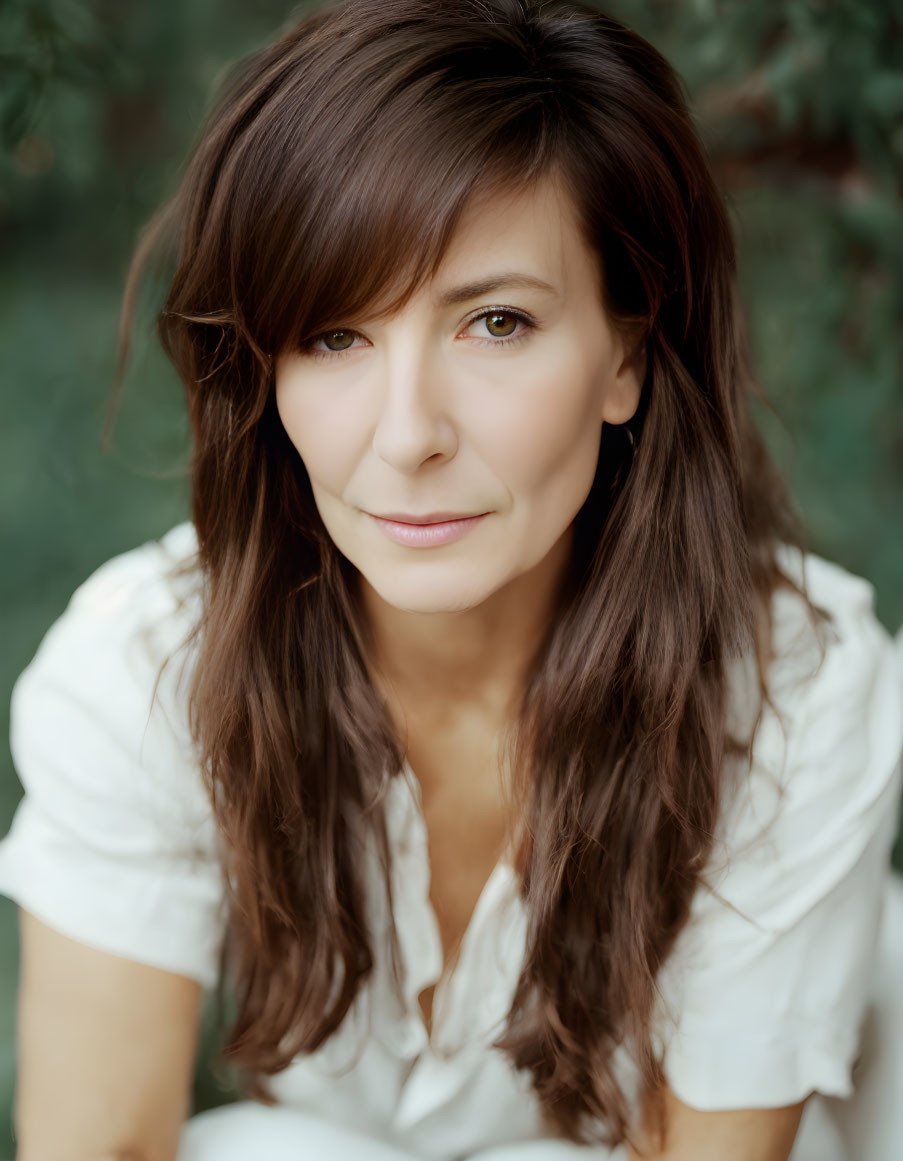 Brown-haired woman in white blouse gazes at camera against green backdrop