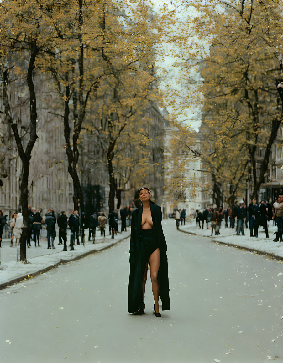 Confident person in black coat on snowy street with autumn trees.