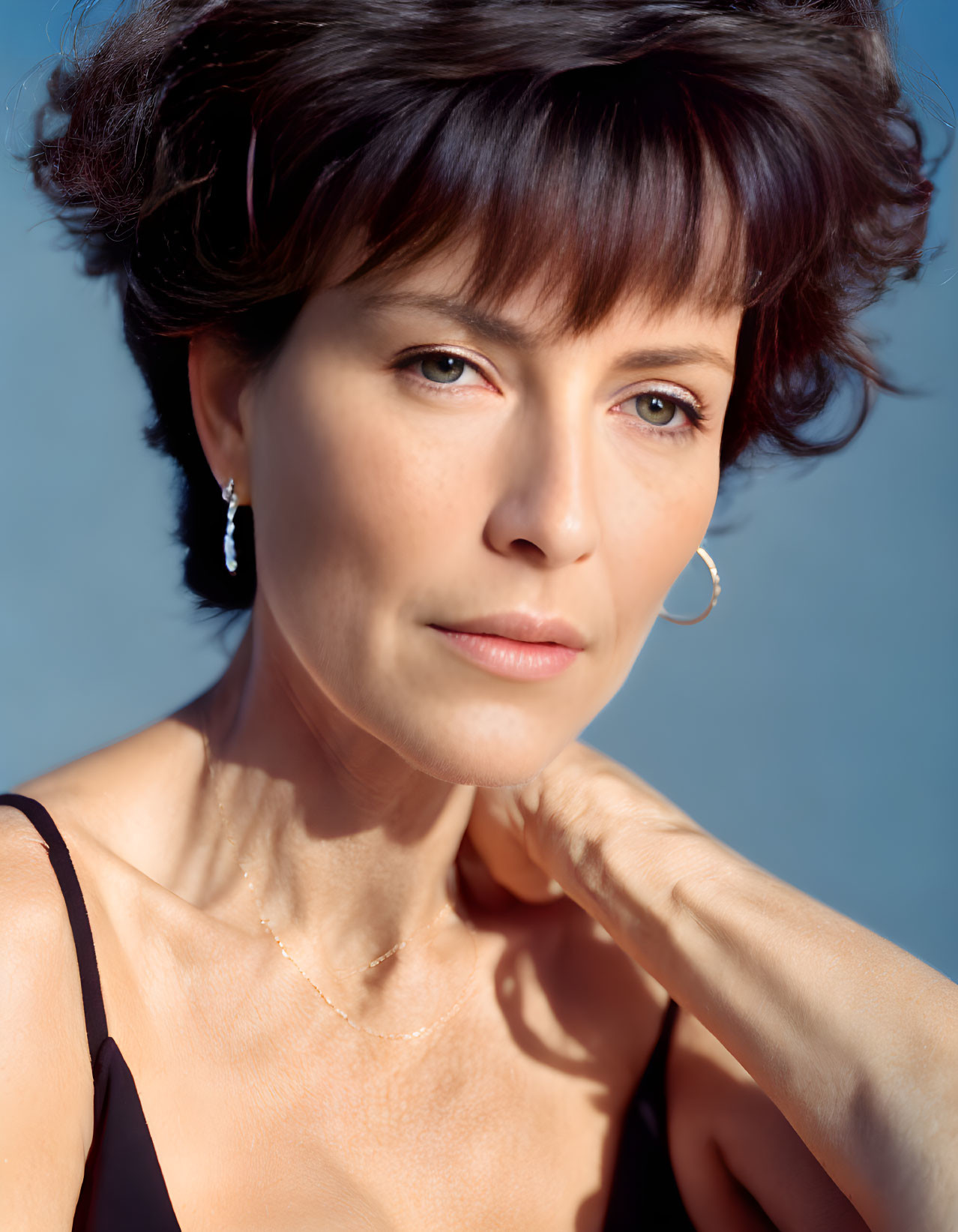 Portrait of woman with short, dark hair in black top on blue background