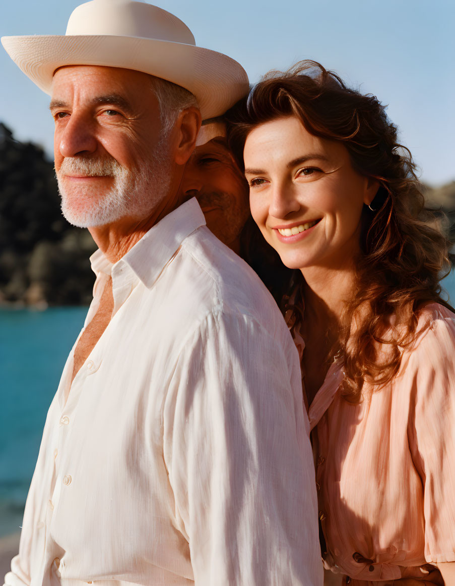 Smiling woman in pink blouse leaning on man in white shirt with blue water backdrop