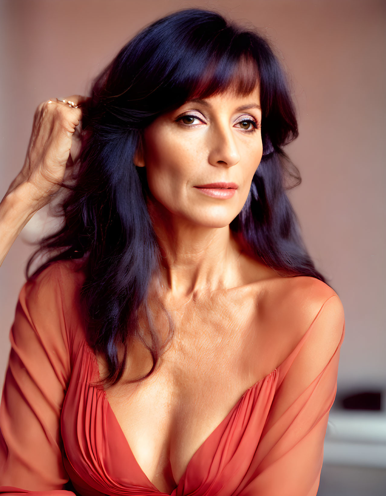 Woman with long dark hair in red v-neck top on pink background