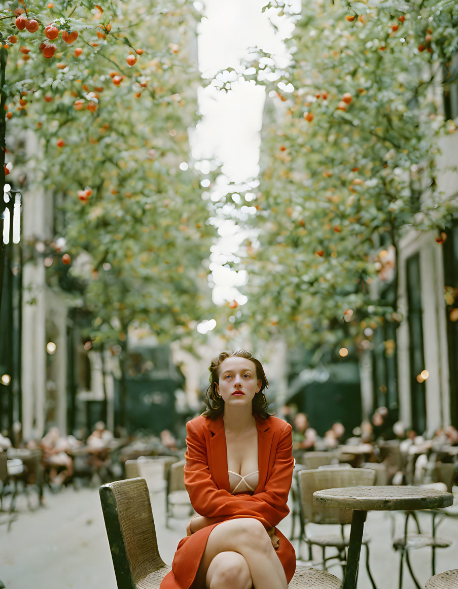 Woman in Orange Dress Alone at Café Table on Cobblestone Street