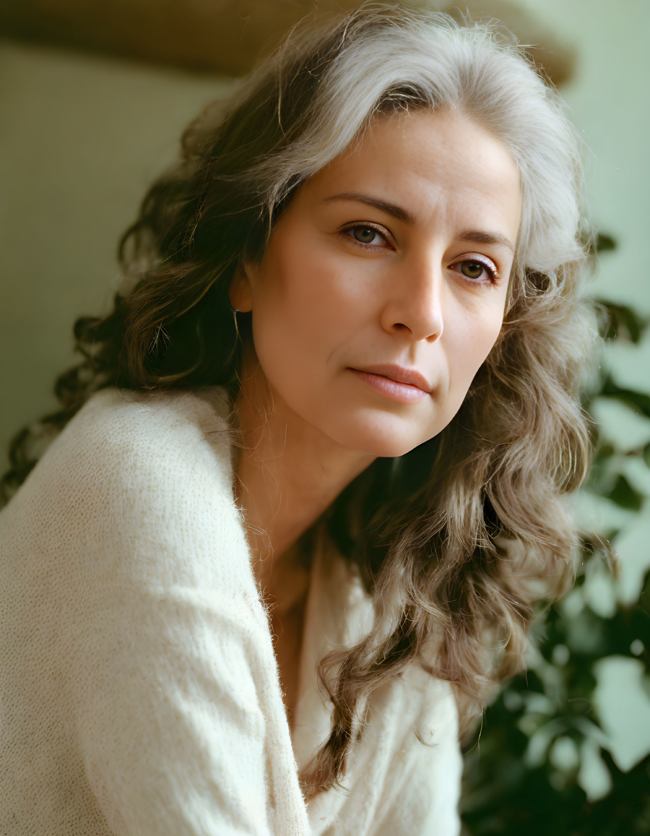 Gray-haired woman in cream sweater gazes against green background