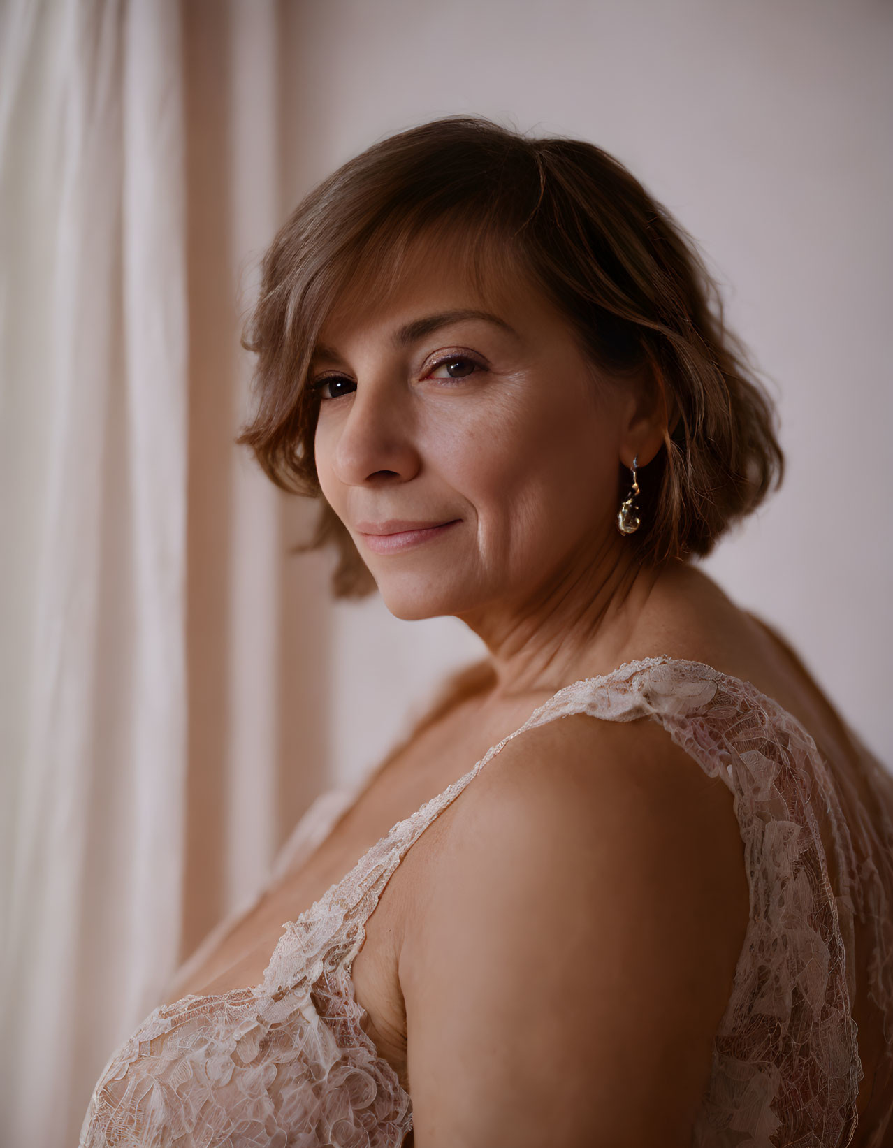 Mature woman in lace garment smiling over shoulder on pink backdrop