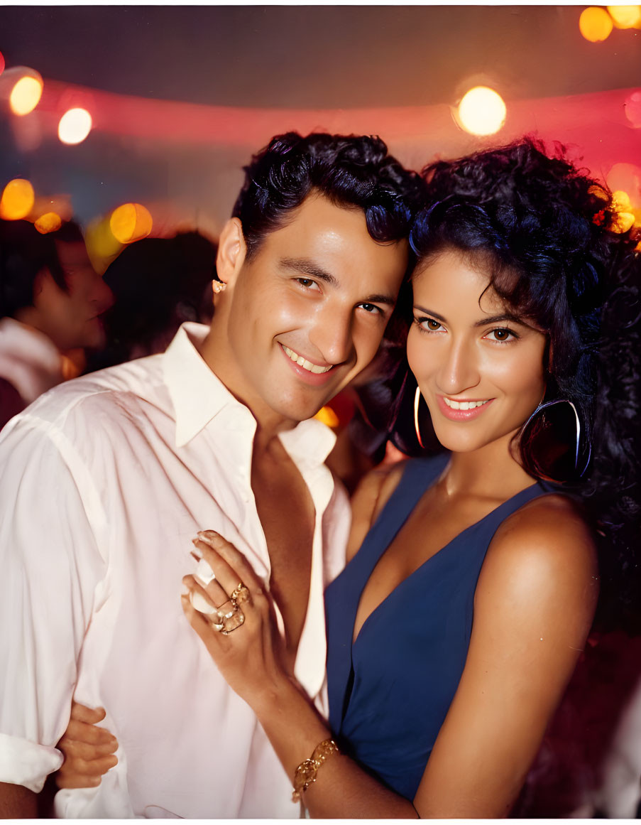 Joyful couple posing at party with warm lighting and guests in background