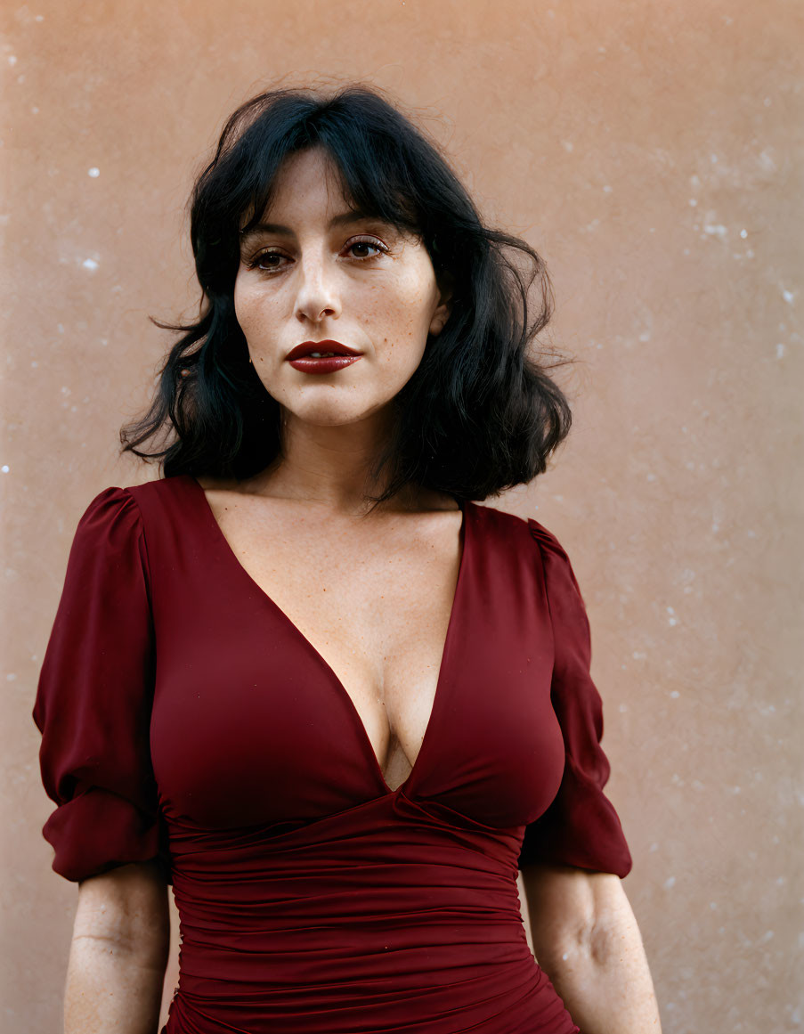 Dark-haired woman in red dress against beige wall