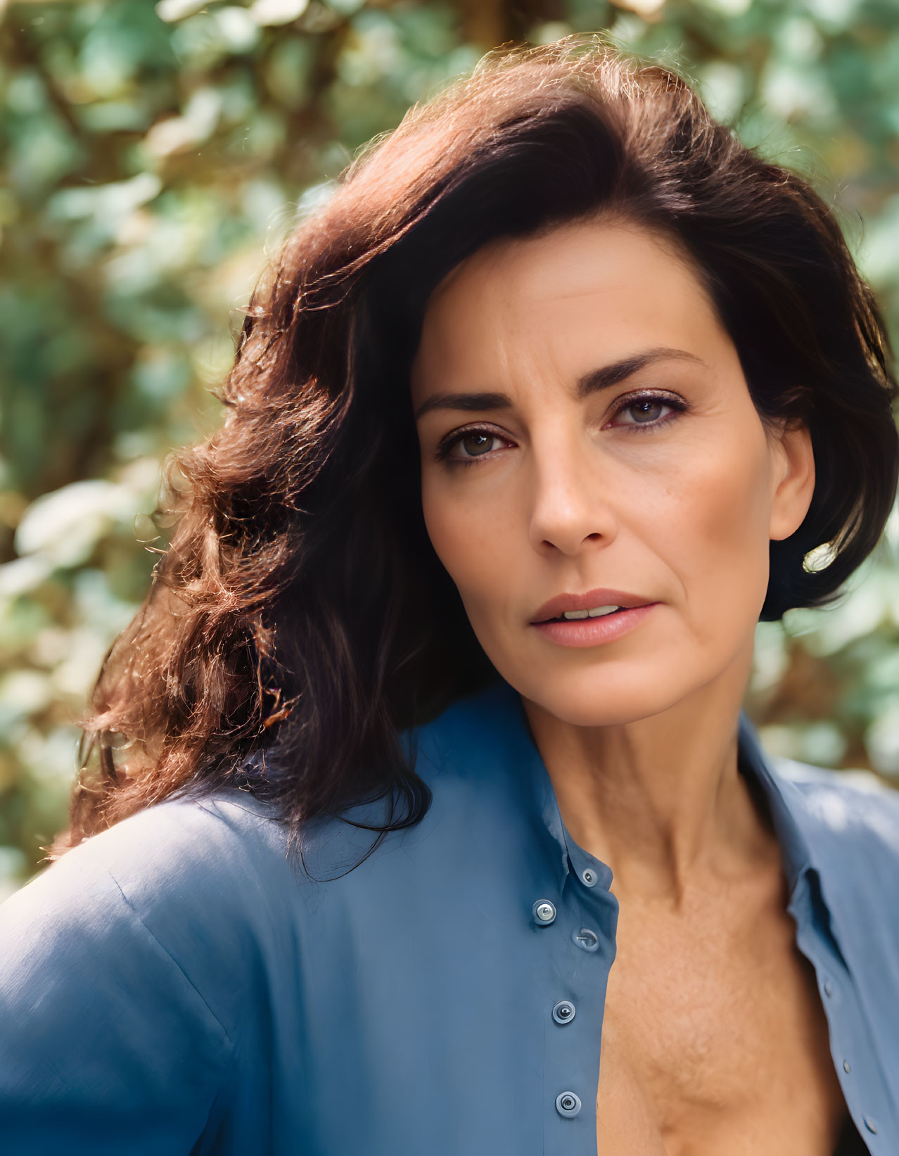 Portrait of woman with dark hair in blue shirt against green foliage