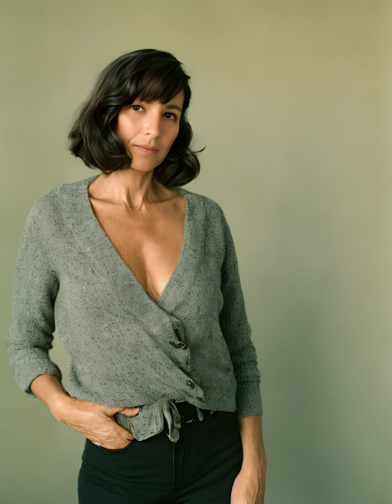 Dark-haired woman in greenish-gray cardigan poses against soft green backdrop