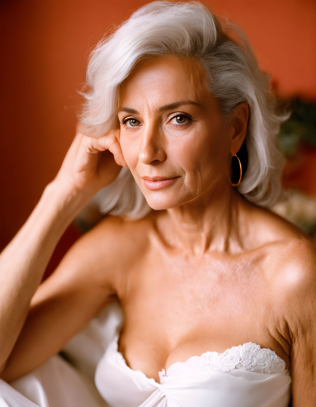 Senior Woman in Silver Hair and Hoop Earrings Poses in White Lace Outfit