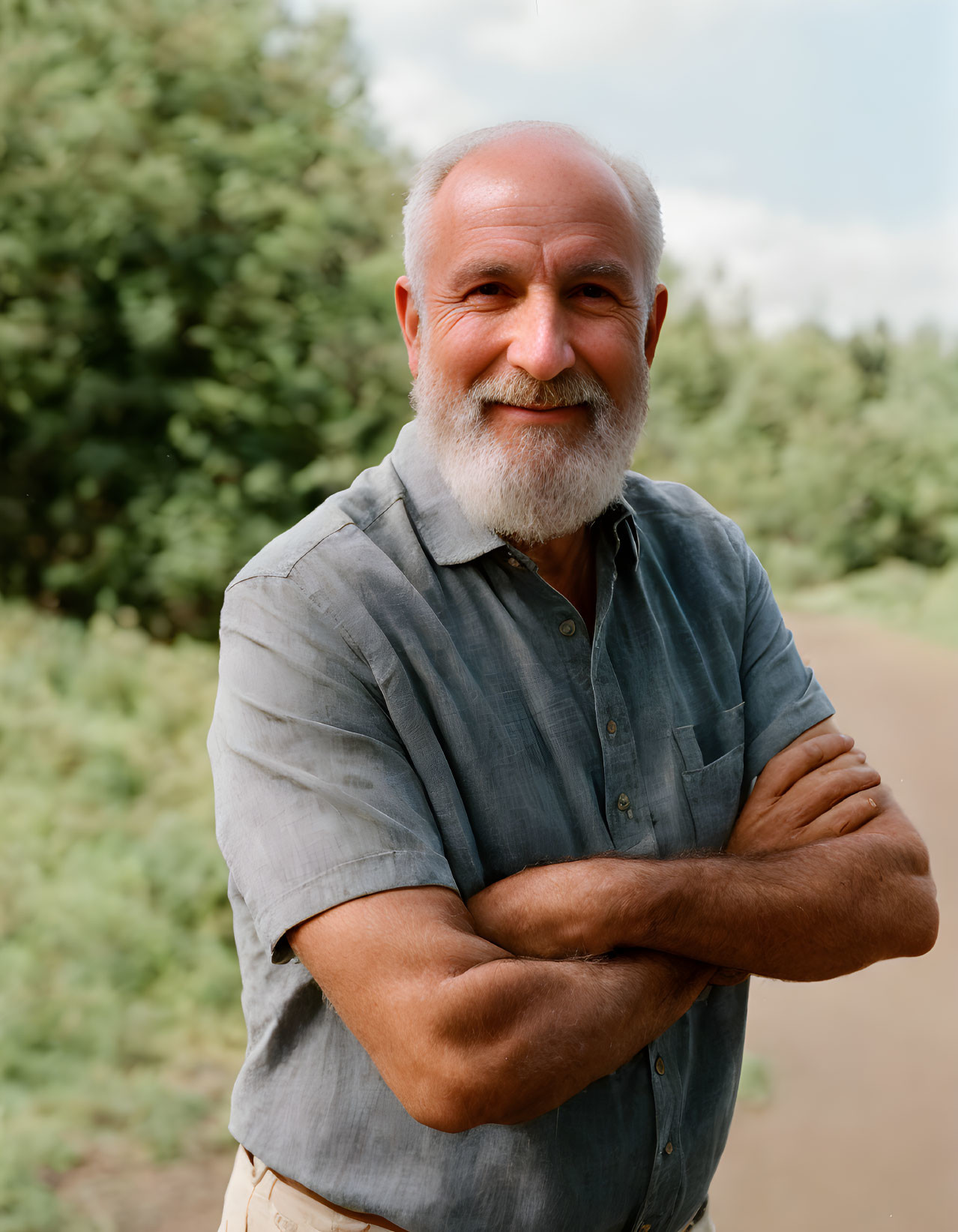 Elderly man with beard smiling outdoors in blue shirt