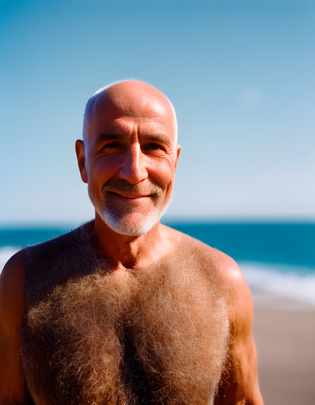 Bald man with gray beard smiling on beach shore