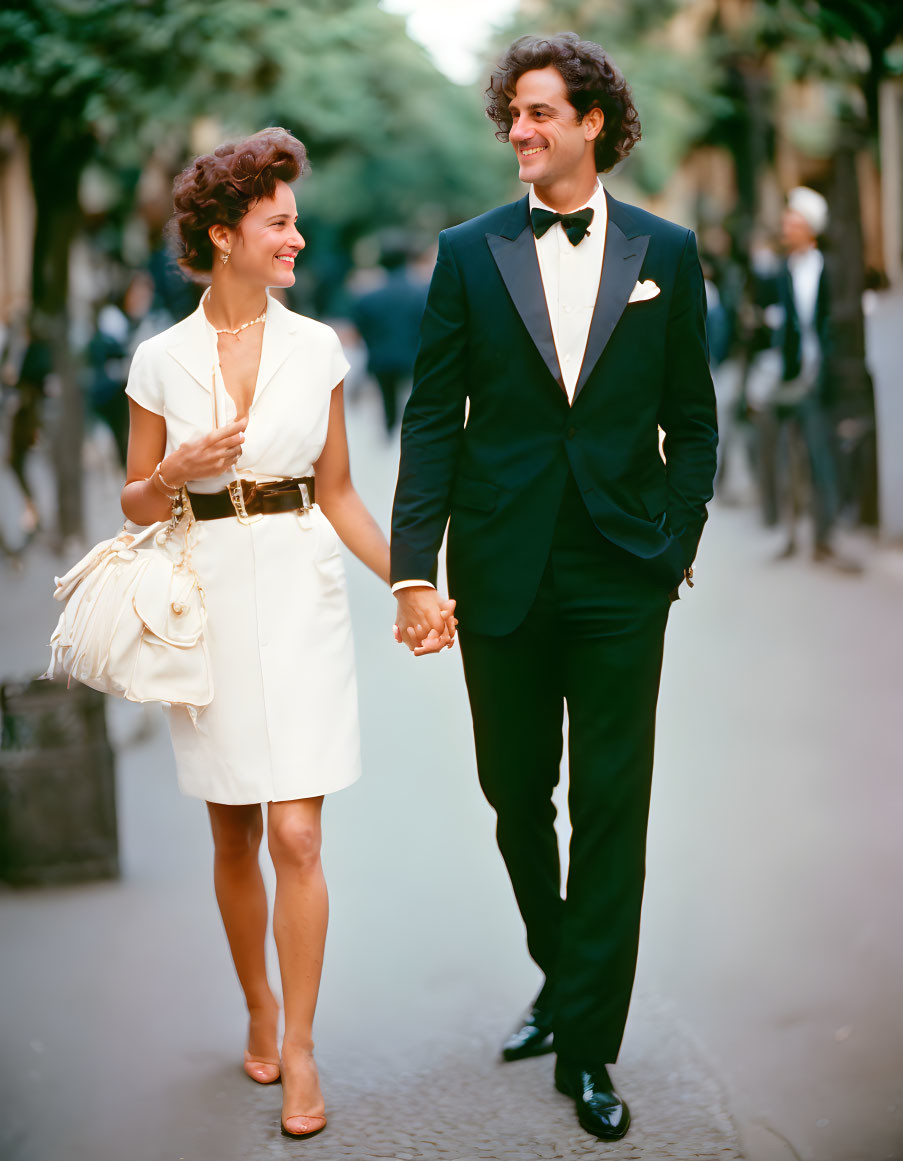 Stylishly dressed couple walking hand in hand down tree-lined street