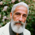 Elderly man with white beard in cream jacket against green foliage