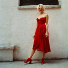 Blonde woman in red dress and boots against pale wall with clutch