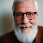 Elderly man with white beard and glasses in brown jacket smiles gently