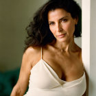 Dark-haired woman in white dress poses by wall with focused expression