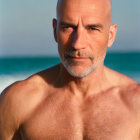 Bald man with beard on beach, shirtless and looking at camera