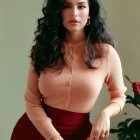 Woman with Long Dark Hair in Peach Top and Maroon Skirt Seated Against Neutral Backdrop