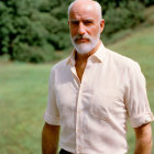 Bald man with beard in light shirt gazes at camera outdoors