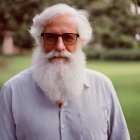 Elderly man with white beard and glasses smiling in light blue shirt