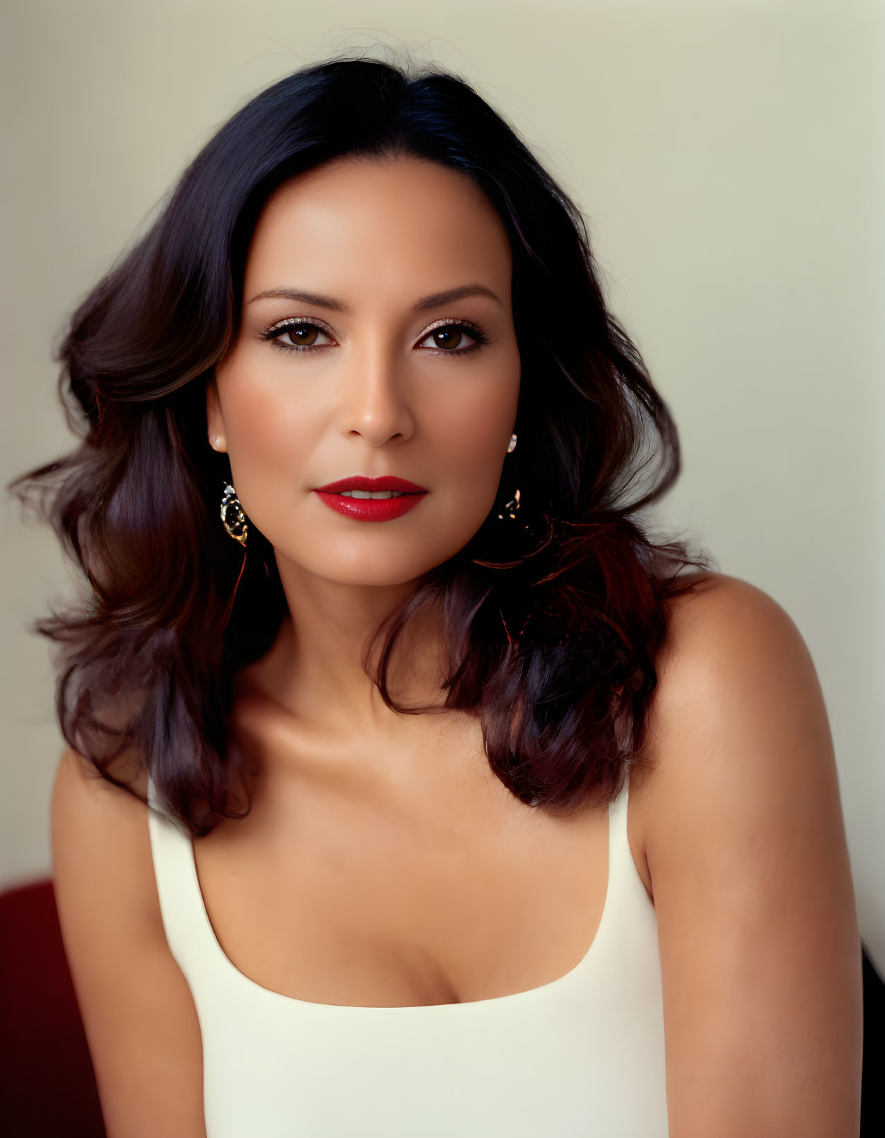 Brown-haired woman in white top with red lipstick and earrings on neutral background