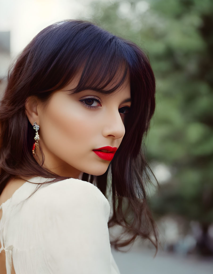 Dark-haired woman in white blouse with red lipstick and earring, looking back.