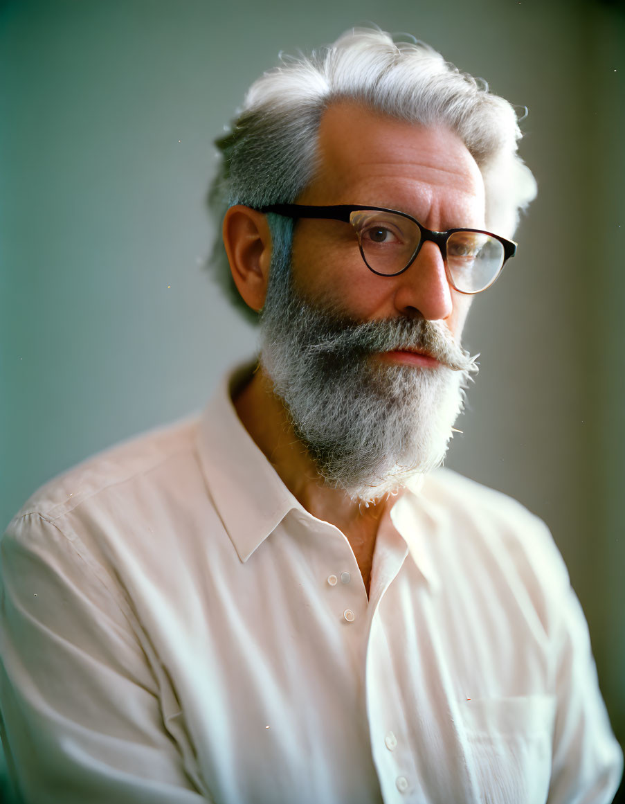 Elderly man with gray beard and glasses in white shirt