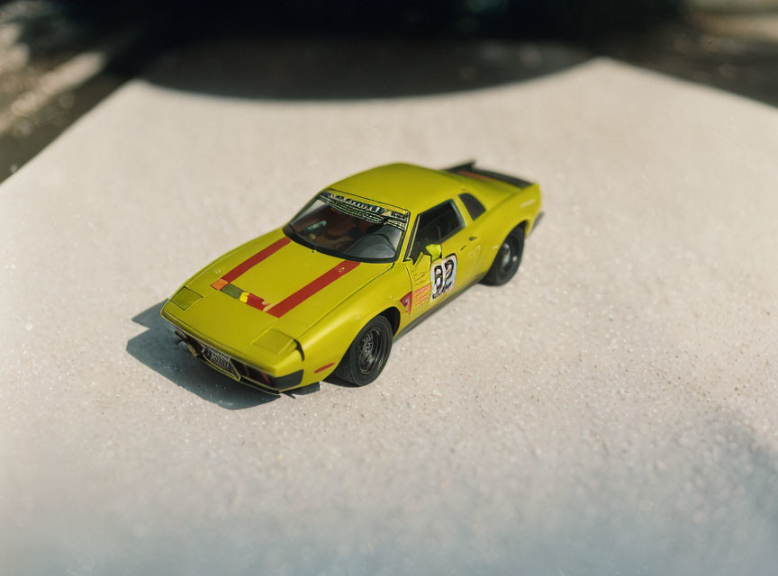 Yellow Toy Race Car with Red Stripes and Number 92 on Textured White Surface