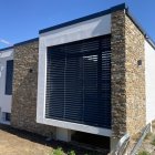 Contemporary house with stone wall accents and large windows in landscaped yard.