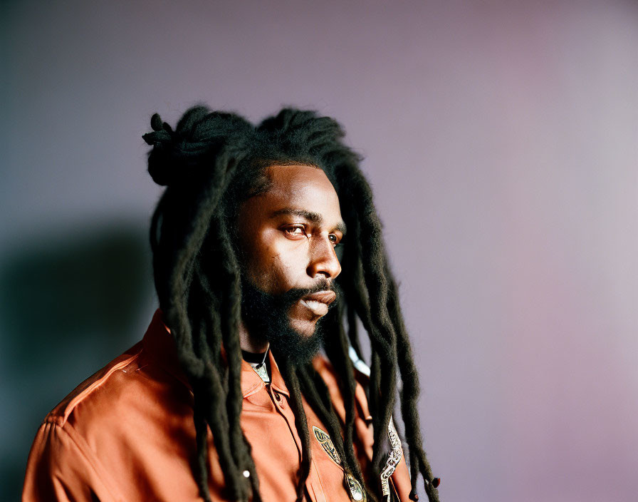 Long dreadlocked man in orange shirt on purple background