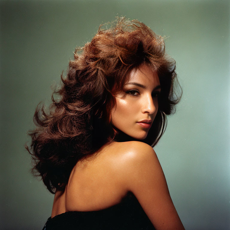 Brown-haired woman with voluminous hair looking back on green background